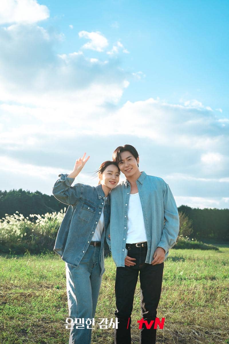 Dua orang berdiri berdekatan di ladang hijau dengan langit biru cerah, mengenakan pakaian denim dan tersenyum ke arah kamera.