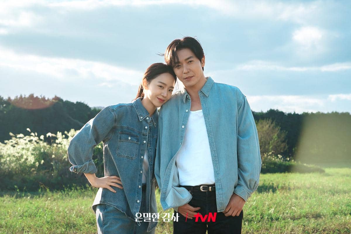 Dua orang berdiri berdekatan di tengah ladang hijau dengan latar langit cerah, keduanya mengenakan pakaian denim biru.