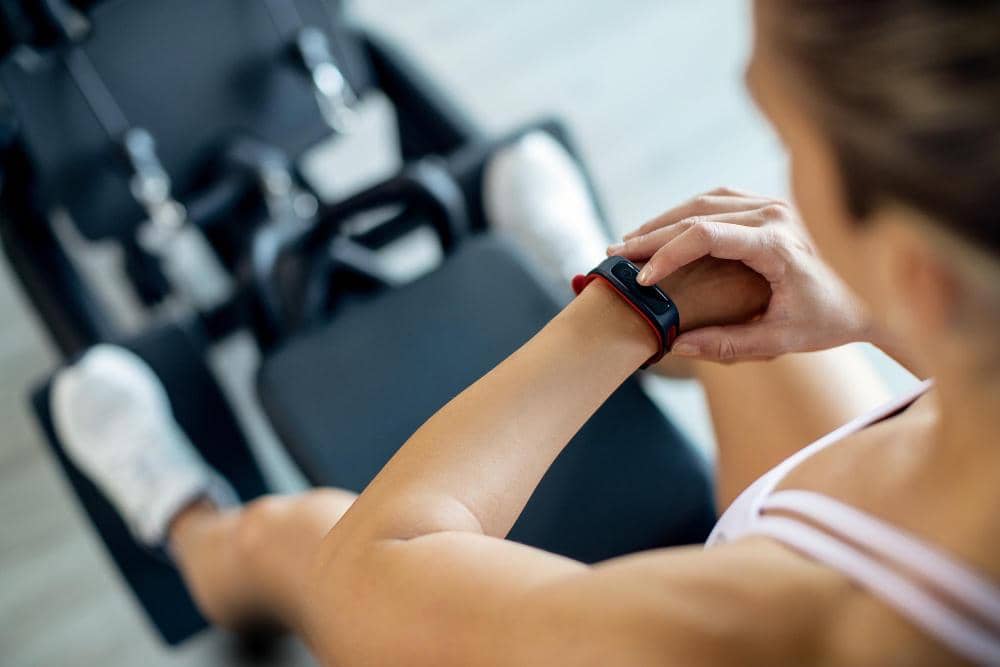 Seorang wanita mengenakan smartwatch sambil berolahraga di gym, memantau aktivitas kebugaran melalui perangkat di pergelangan tangannya.