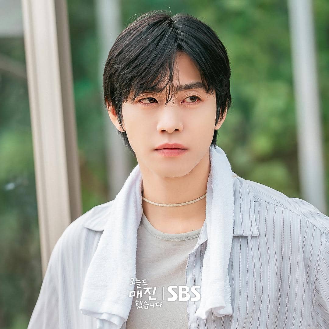 Seorang pria berambut hitam mengenakan kemeja bergaris dan handuk putih di lehernya dalam adegan drama Sold Out On You.