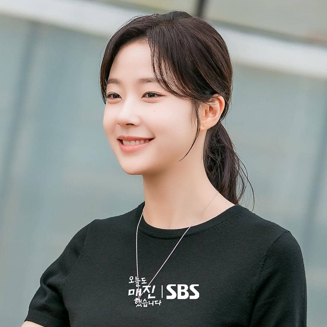 Seorang wanita berambut panjang tersenyum mengenakan kaus hitam dan kalung perak dalam adegan drama Sold Out On You produksi SBS.