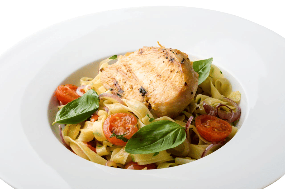 Sepiring pasta dengan potongan ayam panggang, tomat ceri, daun basil segar, dan irisan bawang merah disajikan di atas piring putih.