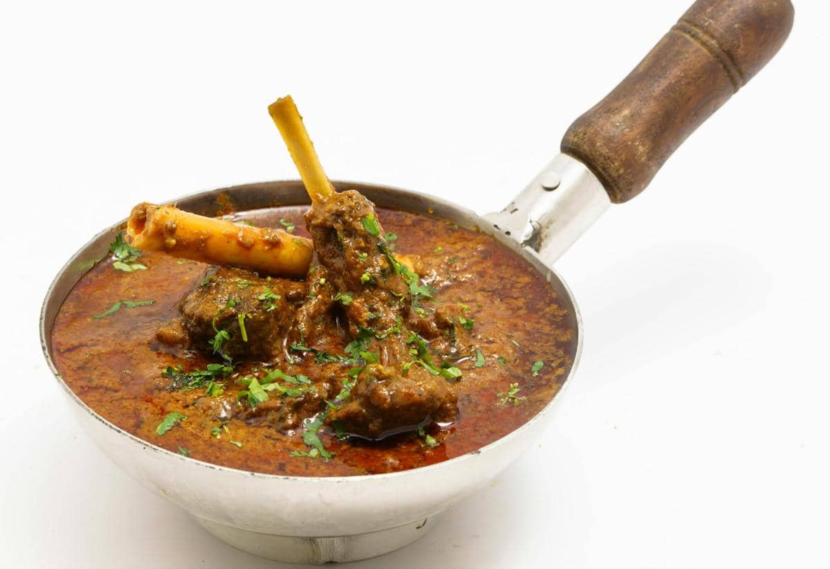 Semangkuk kari kambing berkuah kental berwarna merah kecokelatan dengan potongan daging dan taburan daun ketumbar segar.