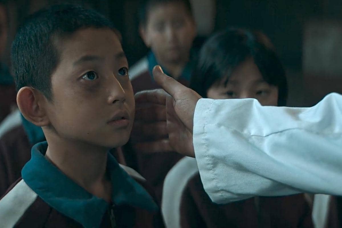 Seorang anak laki-laki berseragam sekolah menatap seseorang yang menyentuh pipinya dalam adegan drama The Wonderfools.