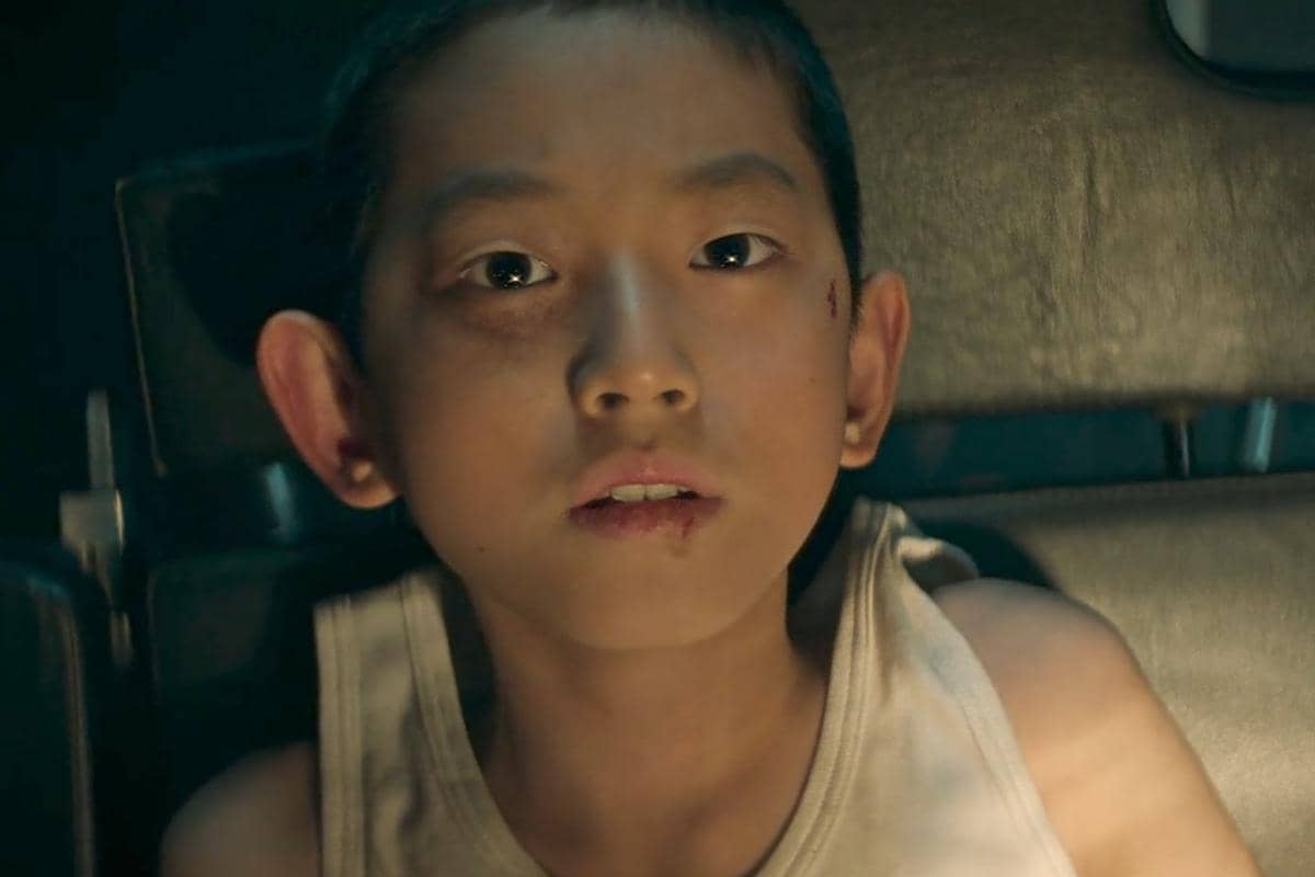 Seorang anak laki-laki dengan wajah terluka dan ekspresi kosong duduk di kursi dalam adegan drama The Wonderfools di Netflix.