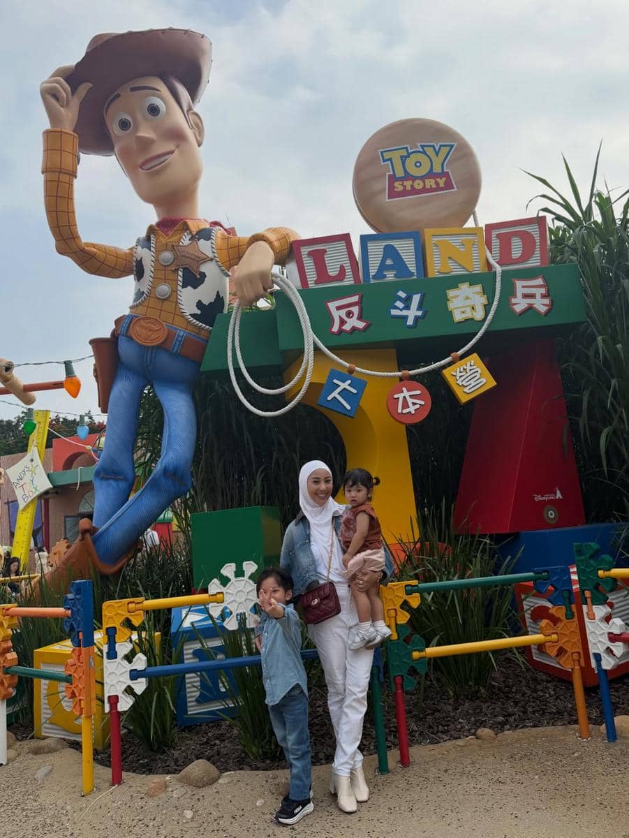 Seorang wanita berhijab berpose bersama dua anak kecil di depan patung besar Woody di area Toy Story Land, Disneyland Hong Kong.