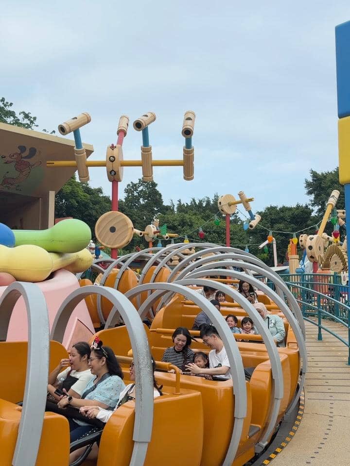 Sejumlah pengunjung menikmati wahana permainan berbentuk kereta oranye di area taman hiburan Disneyland Hong Kong pada siang hari.