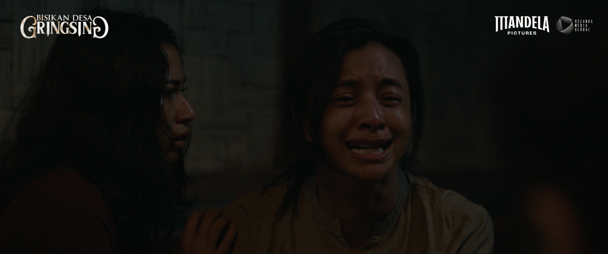 Dua perempuan dalam adegan film Desa Gringsing tampak emosional di ruangan gelap, salah satunya menangis dengan ekspresi ketakutan.