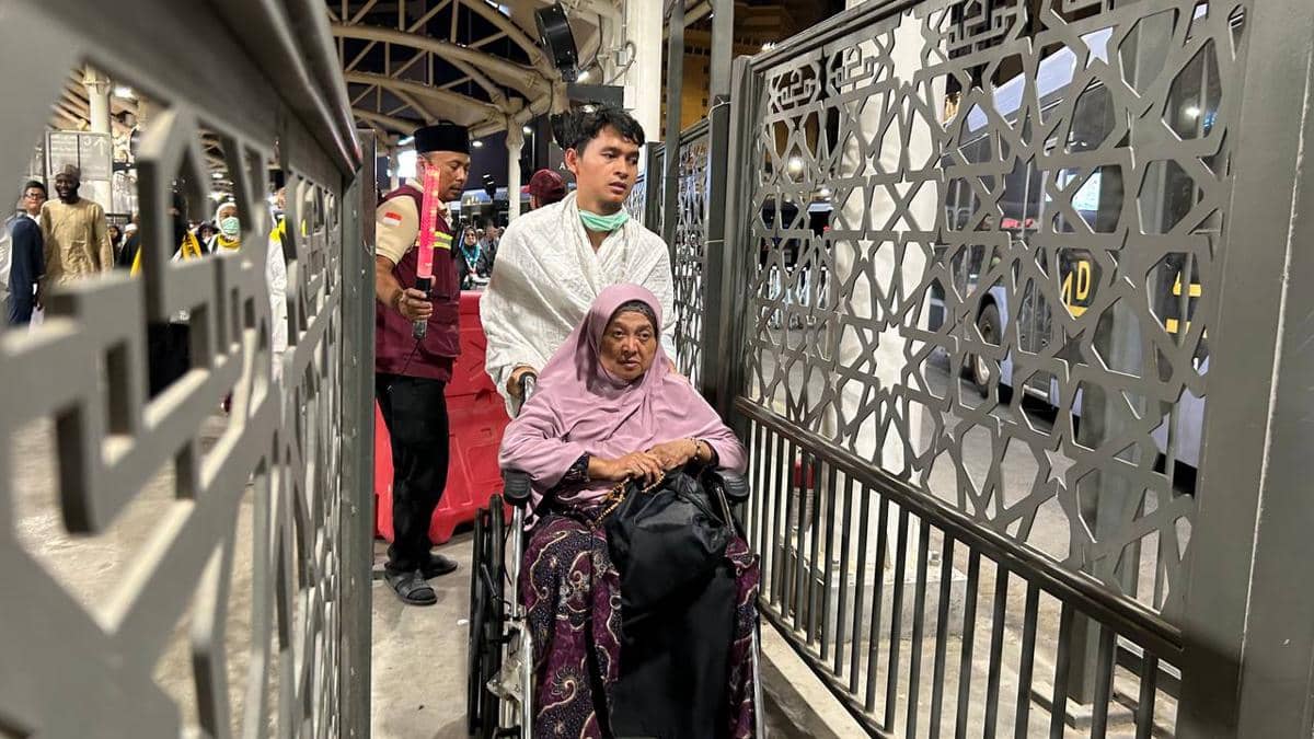 Seorang jemaah perempuan lanjut usia duduk di kursi roda didorong pendamping di gate khusus jemaah berkursi roda Terminal Bus Ajyad, Makkah.