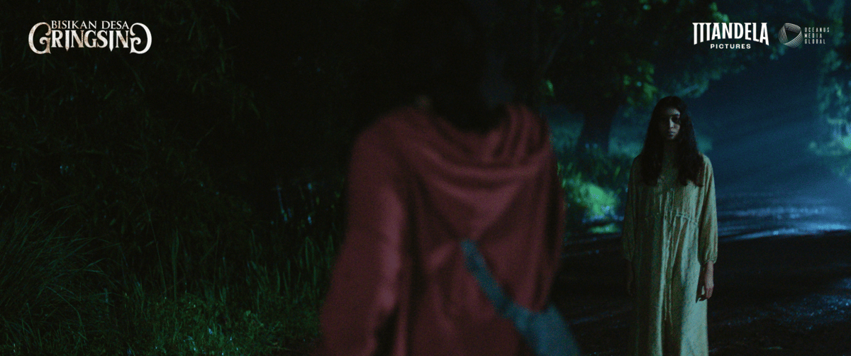 Seorang perempuan bergaun panjang berdiri di jalan gelap berhadapan dengan sosok lain berjaket merah dalam suasana mencekam di malam hari.