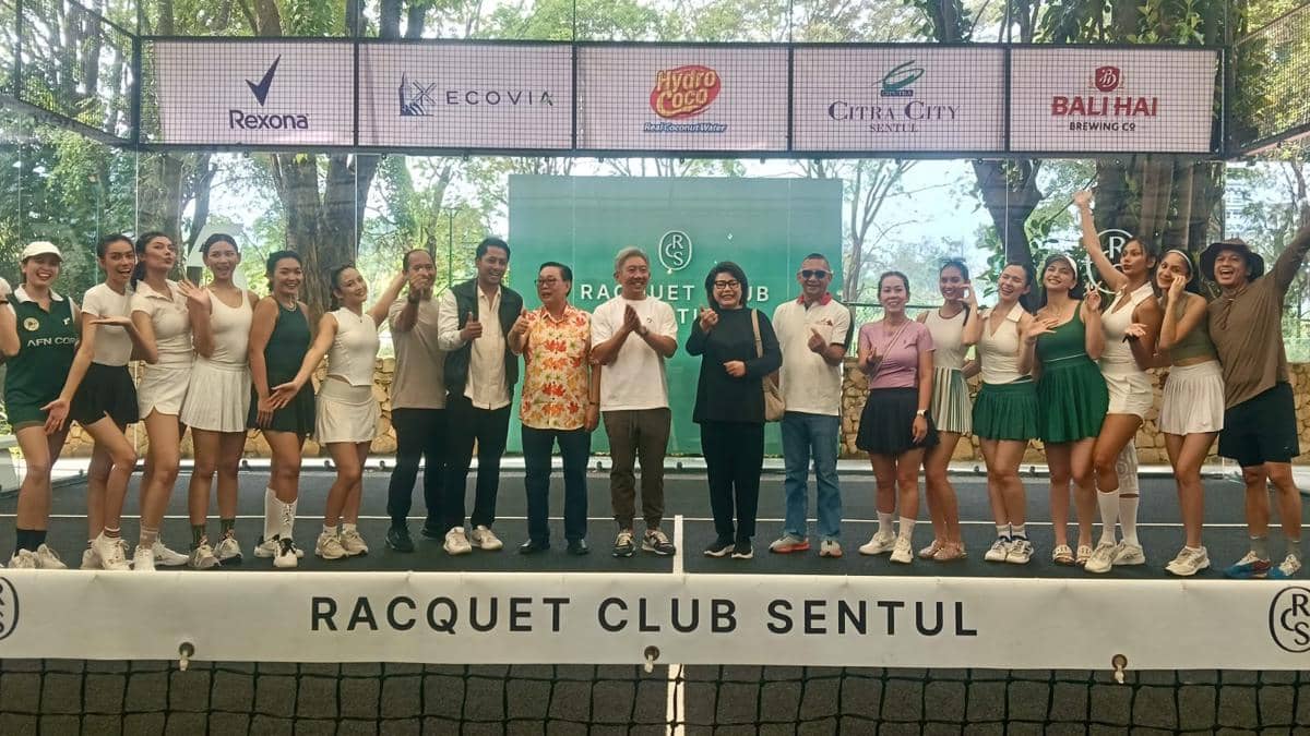 Sejumlah orang berpose bersama di lapangan tenis dengan latar belakang papan bertuliskan Racquet Club Sentul dan logo sponsor.
