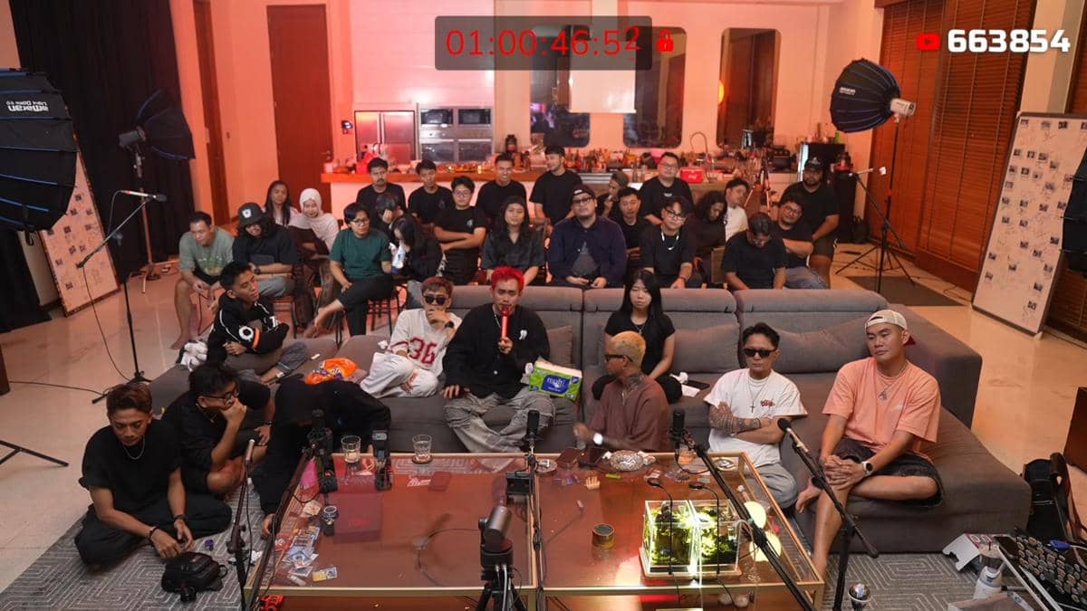 Sekelompok orang duduk di ruang tamu dengan pencahayaan hangat, beberapa berbicara di depan mikrofon dan kamera untuk acara siaran langsung.