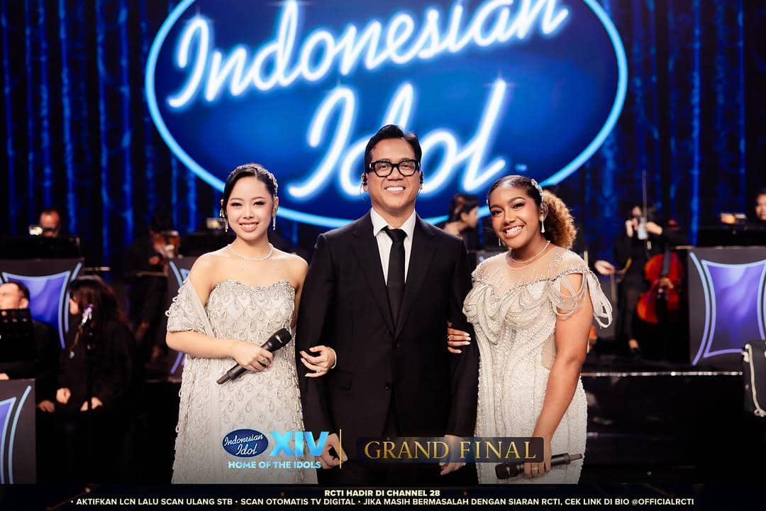 Tiga orang berdiri di panggung Indonesian Idol Season 14 mengenakan busana formal pada malam Grand Final dengan latar logo besar biru.