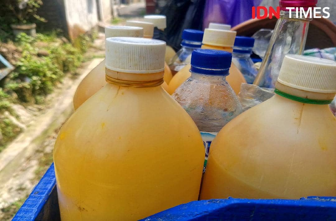 Beberapa botol berisi jamu tradisional berwarna kuning dengan tutup putih dan biru tersusun di wadah biru di area luar rumah.