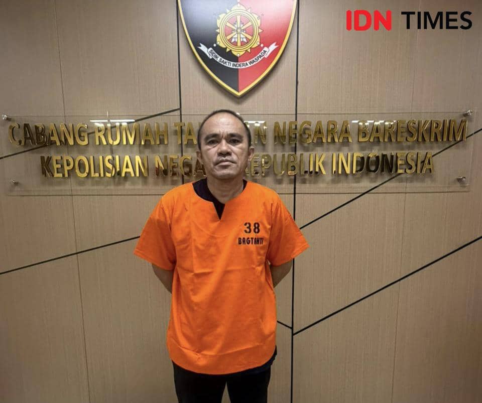 Seorang pria mengenakan baju tahanan oranye dengan nomor 38 berdiri di depan papan bertuliskan Cabang Rumah Tahanan Negara Bareskrim Polri.