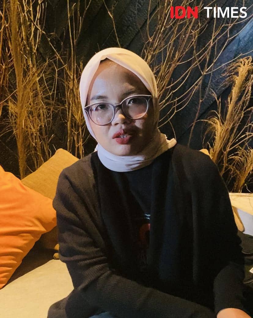 Seorang perempuan berhijab dan berkacamata duduk di sofa dengan latar dekorasi ranting kering di MD Palace.