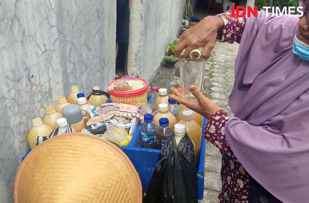 Seorang penjual jamu tradisional menuangkan minuman herbal ke dalam gelas di atas gerobak berisi botol jamu di Purwokerto Timur.