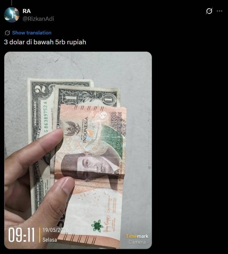 Seseorang memegang uang kertas 5.000 rupiah dan dua lembar dolar Amerika Serikat satuan 1 dolar di atas permukaan abu-abu.