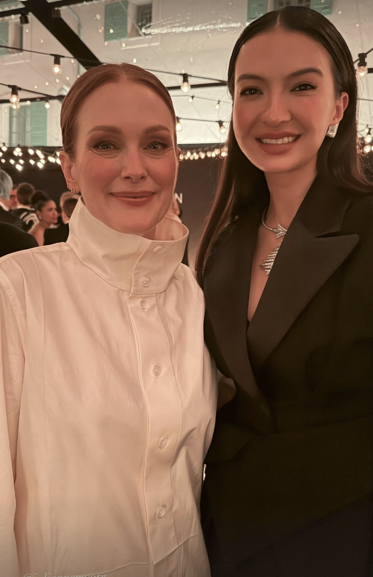 Dua perempuan berpose bersama di acara malam dengan pencahayaan hangat, mengenakan busana elegan berwarna putih dan hitam.