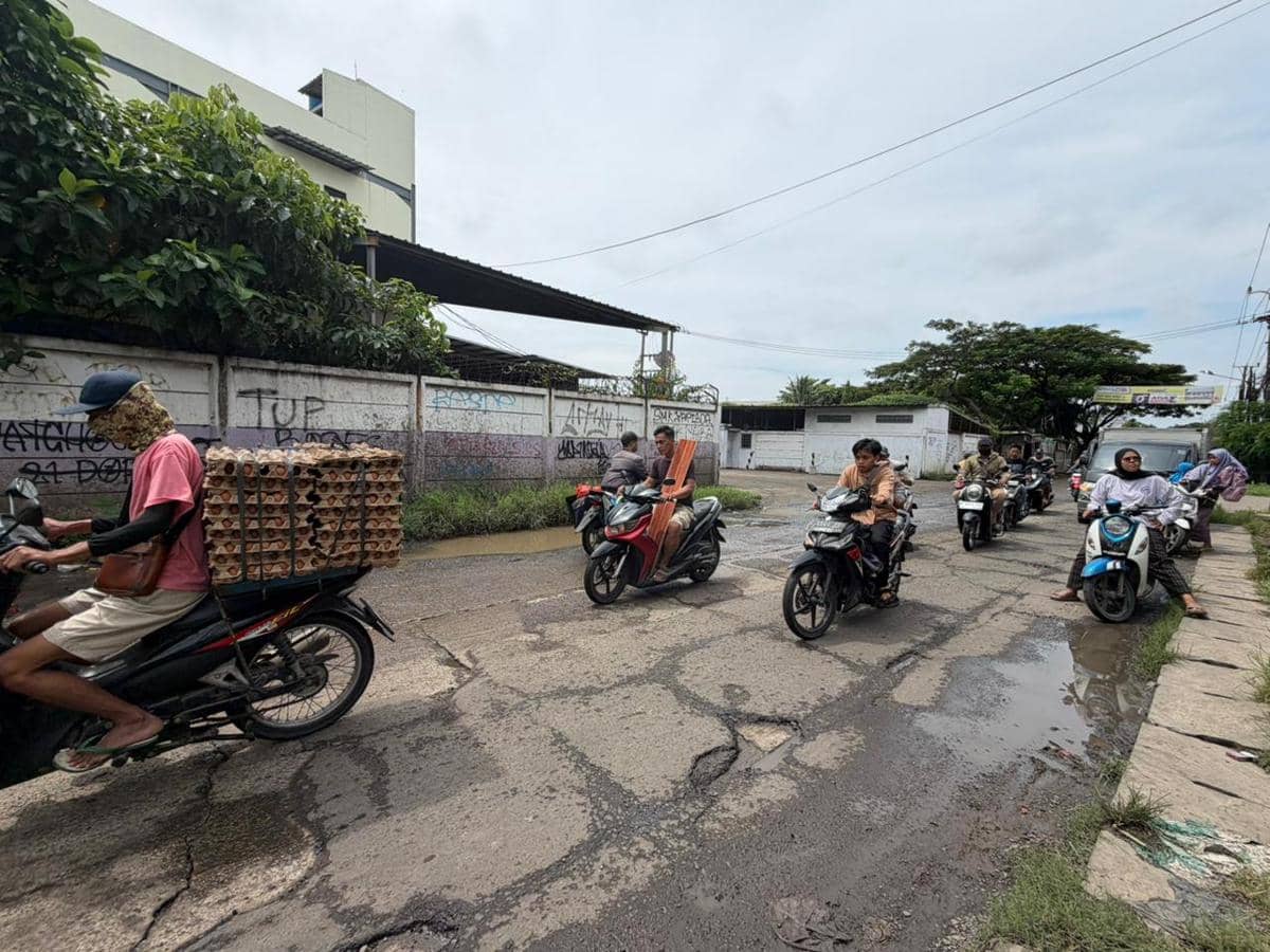 Sejumlah pengendara motor melintasi jalan rusak dan berlubang di kawasan Rajeg-Mauk, Tangerang, dengan genangan air di beberapa titik.