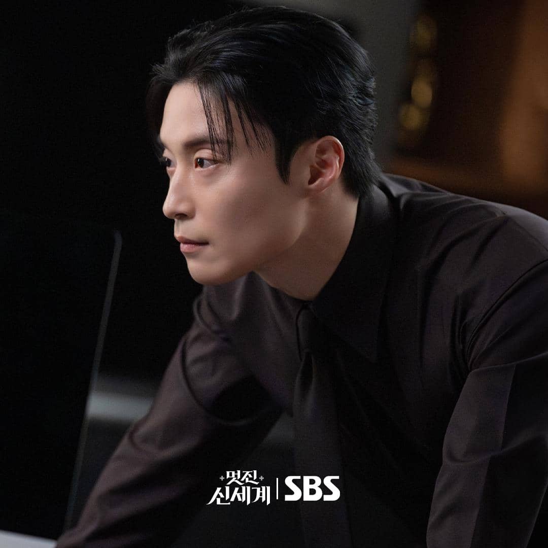 Seorang pria berpenampilan rapi mengenakan kemeja hitam sedang menatap serius ke arah depan dalam adegan drama My Royal Nemesis.