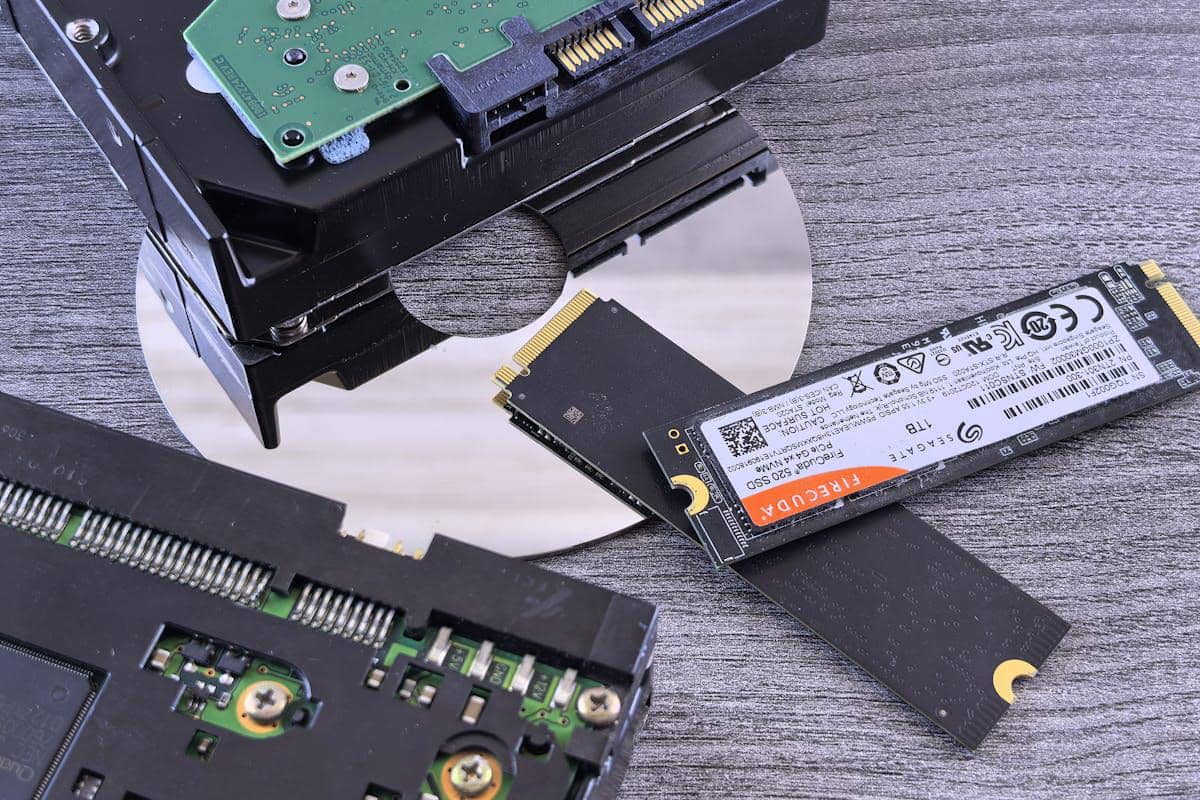 Beberapa perangkat penyimpanan data seperti SSD M.2 dan hard disk diletakkan di atas permukaan kayu abu-abu.