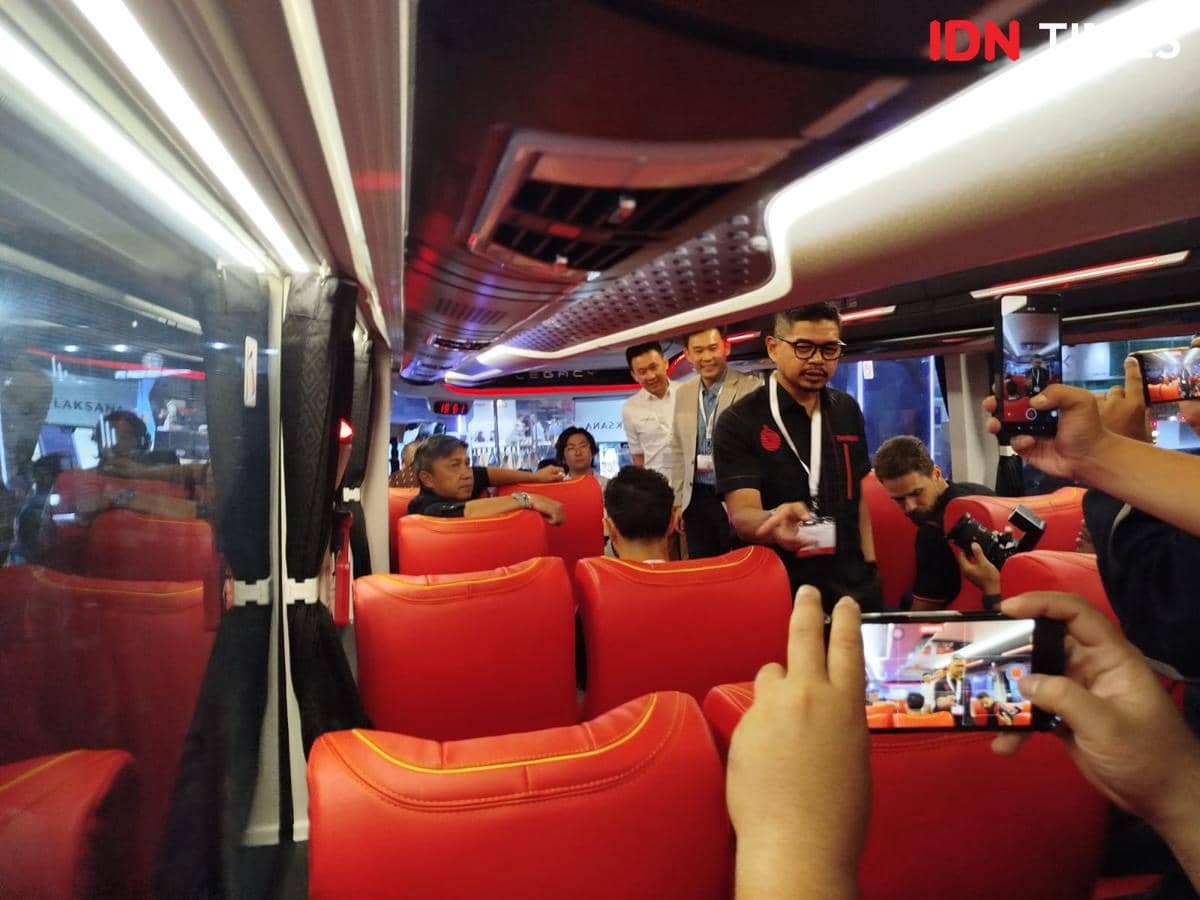Beberapa orang berada di dalam bus listrik baru dengan kursi merah, sebagian mengambil foto menggunakan ponsel di area kabin.