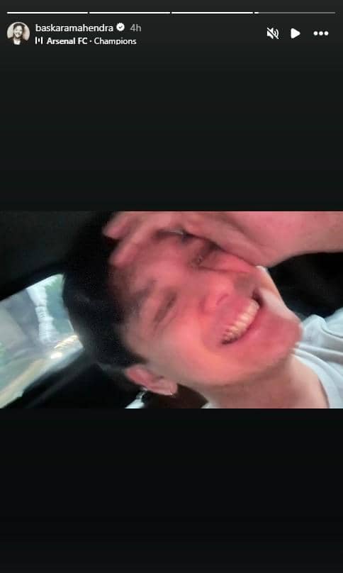 Seorang pria tersenyum lebar sambil menutup sebagian wajahnya dengan tangan di dalam mobil, tampak bahagia merayakan kemenangan Arsenal.