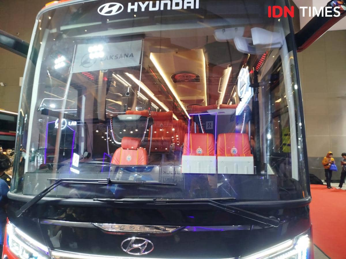 Bus listrik Hyundai dengan interior kursi berwarna merah dan logo Persija Jakarta dipamerkan di sebuah acara otomotif dalam ruangan.
