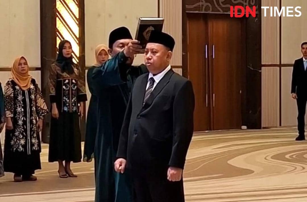 Seorang pria mengenakan setelan jas hitam mengucap sumpah jabatan dengan kitab suci di atas kepalanya dalam upacara pelantikan.