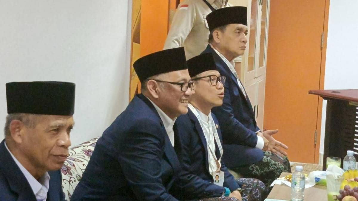 Sejumlah pejabat dan tokoh nasional mengenakan jas biru dan peci hitam duduk berdampingan di dalam ruangan saat acara resmi.