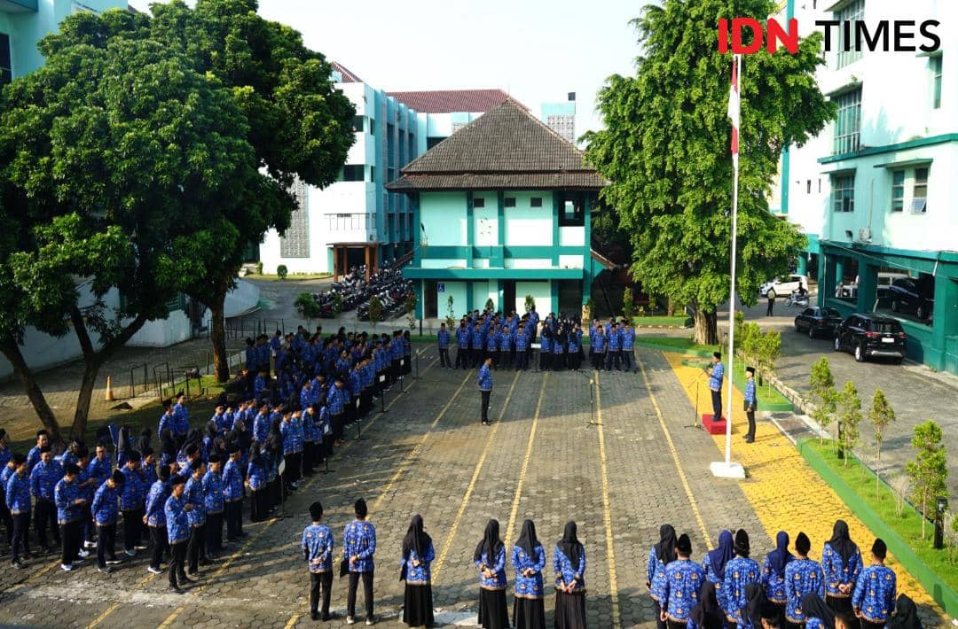 Upacara bendera di halaman kampus UIN Saizu dengan peserta mengenakan seragam biru berbaris rapi menghadap tiang bendera.