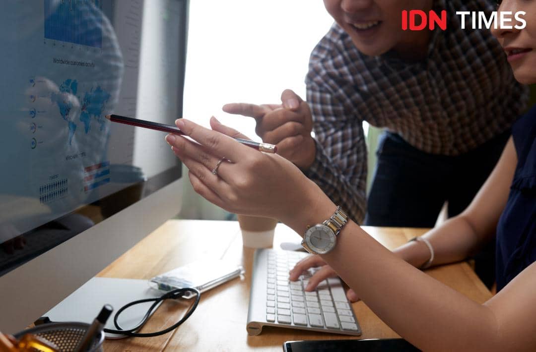 Dua orang bekerja di depan komputer sambil menganalisis data digital di layar, menunjukkan kolaborasi dalam proses digitalisasi.