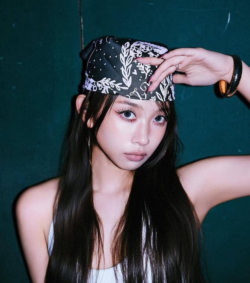 Seorang perempuan berambut panjang mengenakan bandana hitam bermotif putih dan atasan tanpa lengan berwarna terang di latar belakang gelap.