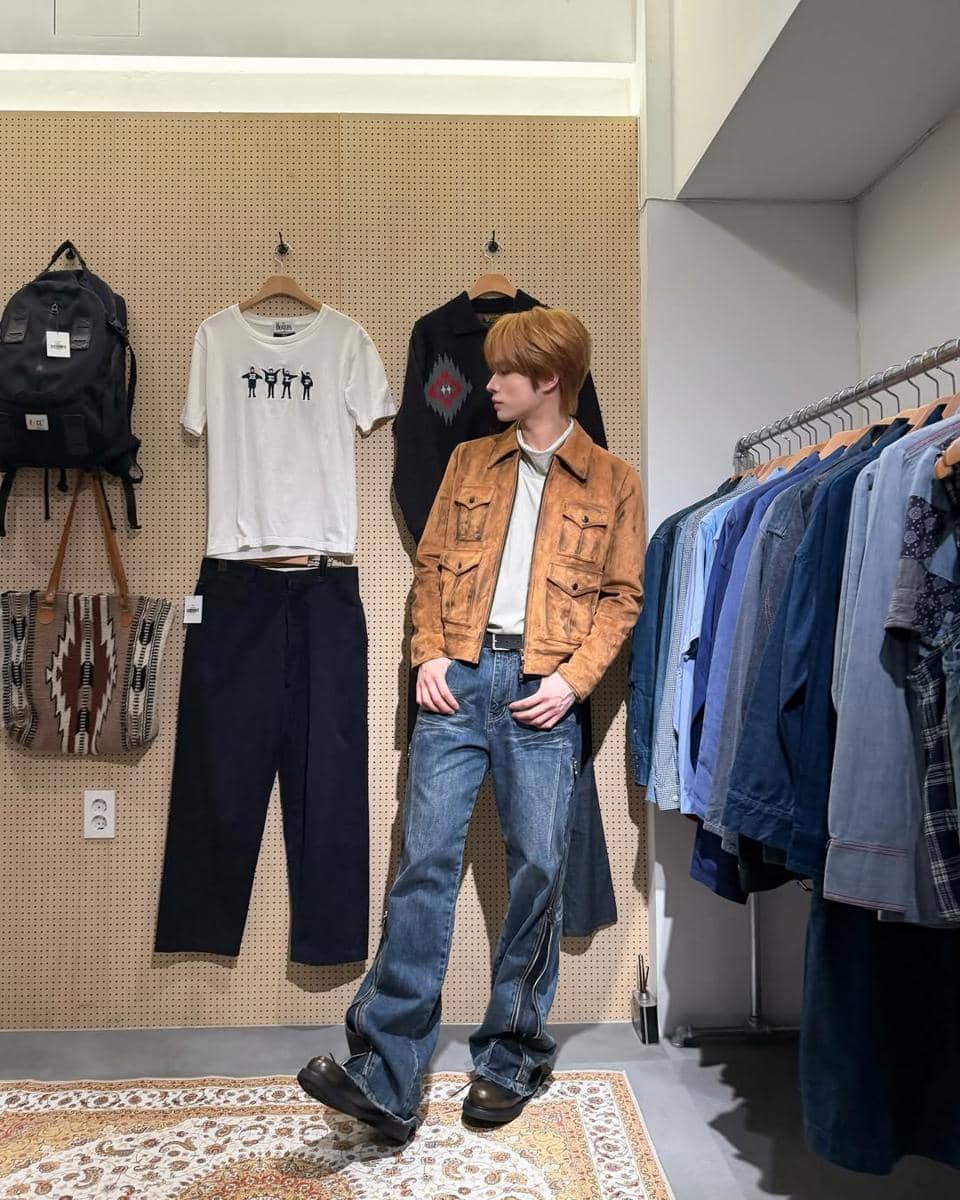 Seorang pria bergaya street style mengenakan jaket cokelat suede dan celana jeans longgar di dalam toko pakaian kasual.