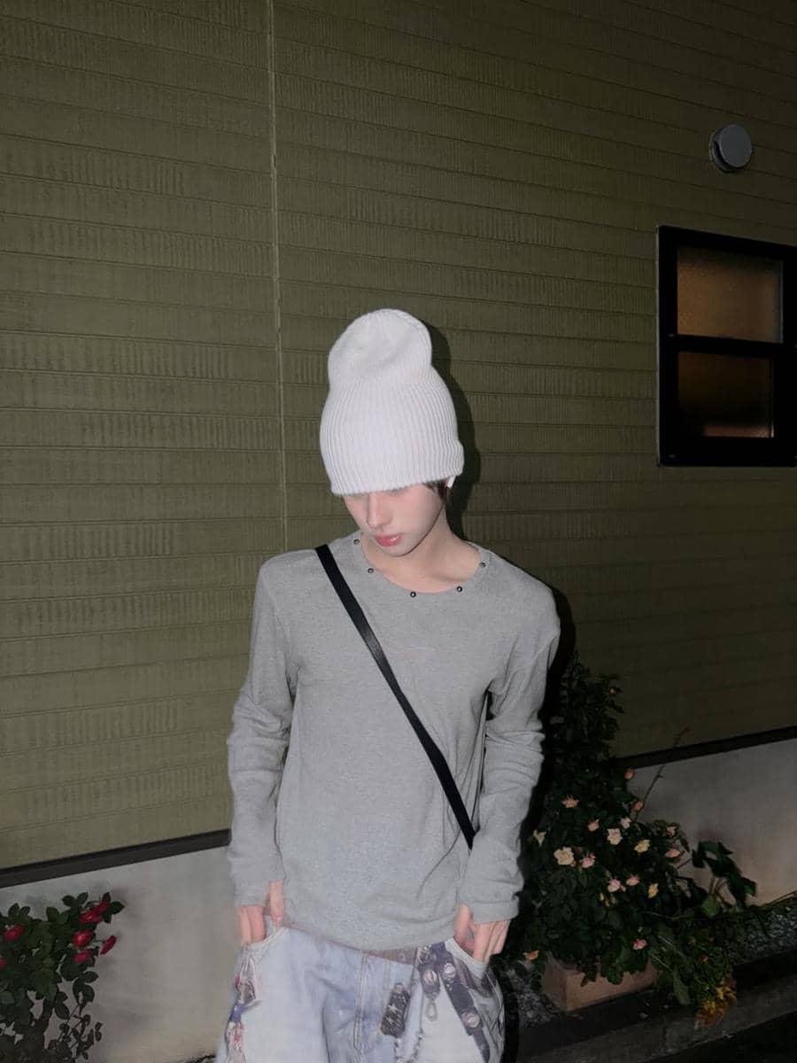 Seorang pria mengenakan beanie putih, kaus abu-abu panjang, dan celana longgar dengan gaya street style di malam hari.