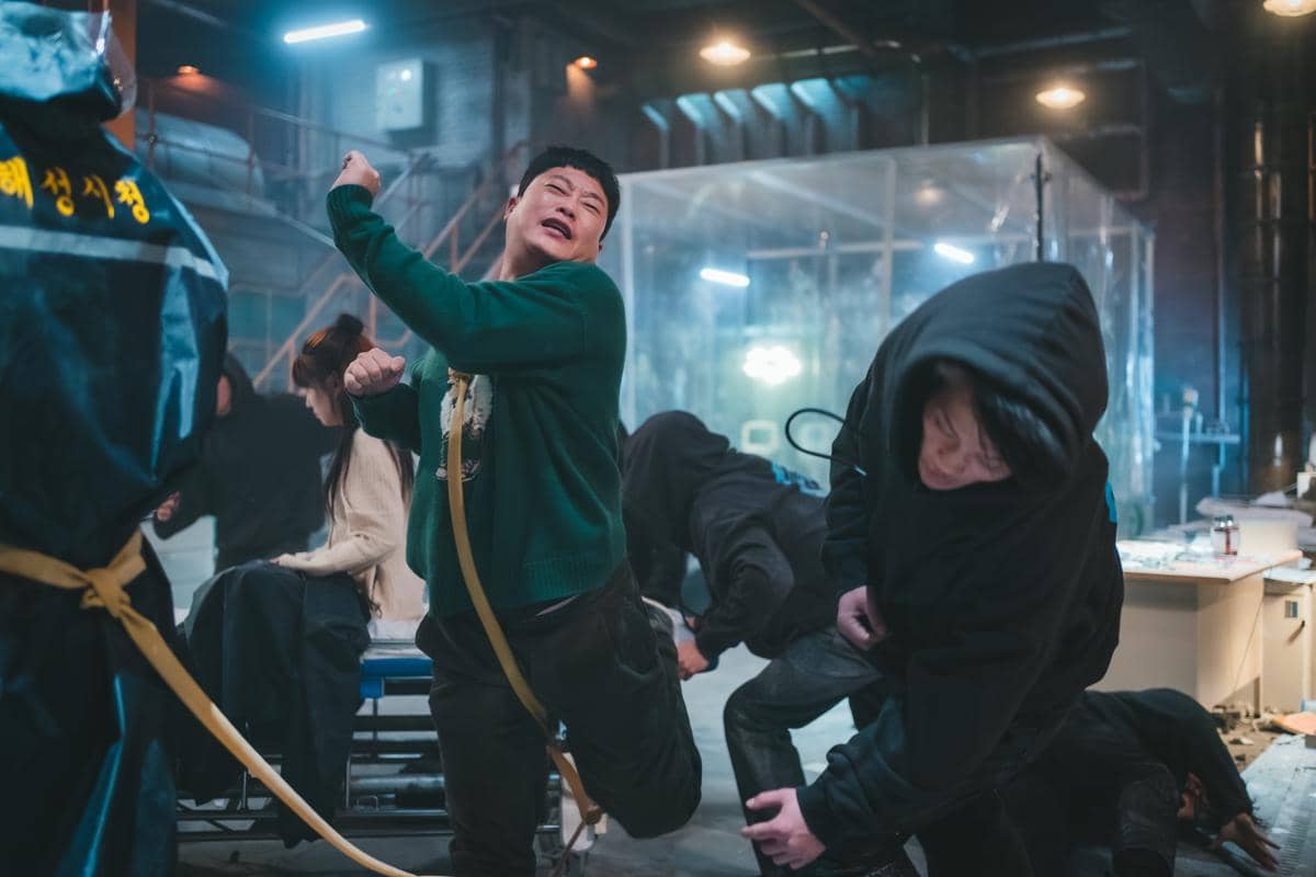 Adegan aksi intens dalam drama The WONDERfools memperlihatkan beberapa karakter bertarung di ruangan industri dengan pencahayaan biru redup.