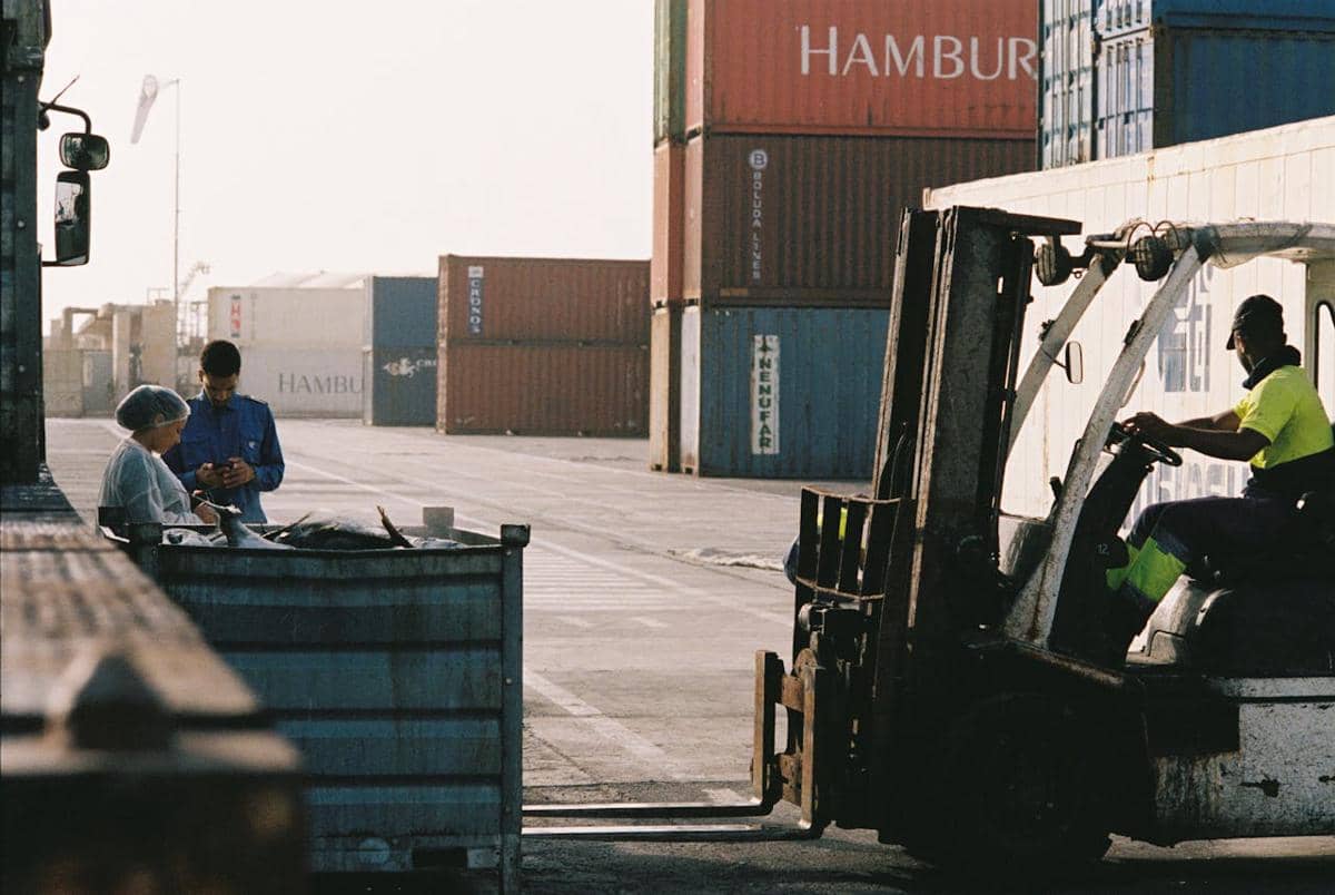 ilustrasi para pekerja mengoperasikan forklift di area penyimpanan kontainer