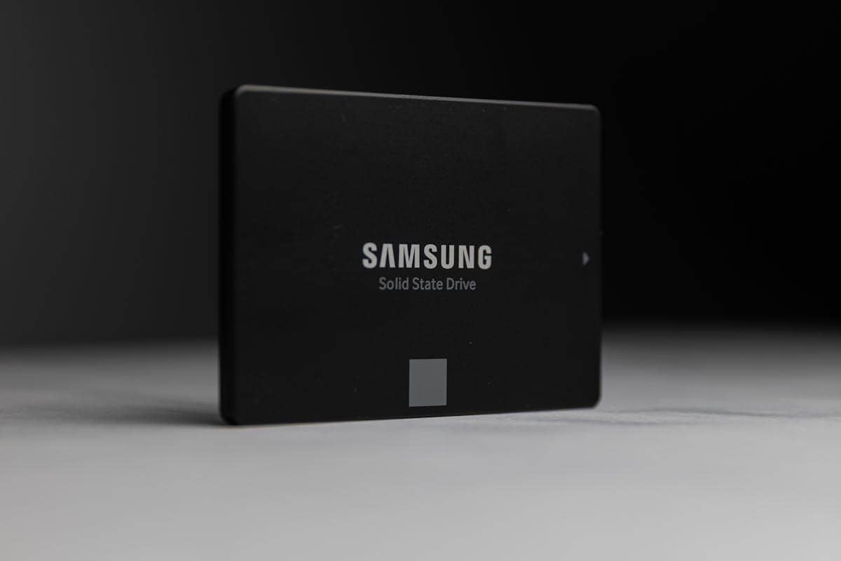 SSD Samsung berwarna hitam dengan tulisan 'Solid State Drive' terlihat berdiri di atas permukaan abu-abu dengan latar belakang gelap.
