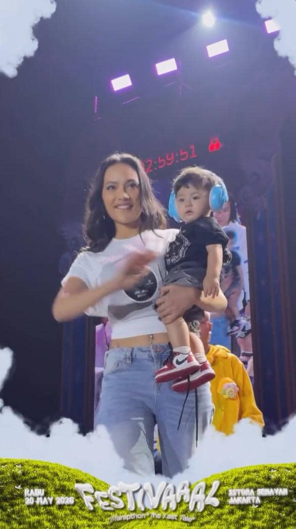 Seorang wanita mengenakan kaus putih dan celana jeans memegang anak kecil dengan pelindung telinga di acara Festivaaal Marapthon: The Last Tale.