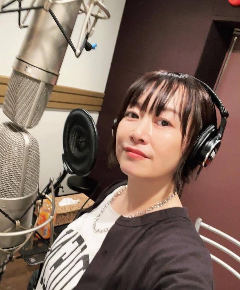 Seorang perempuan mengenakan headphone berpose di depan mikrofon besar di dalam studio rekaman dengan latar dinding berwarna gelap.