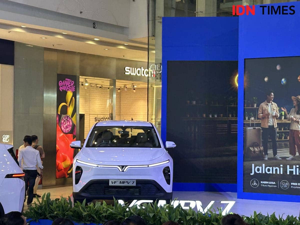 Mobil VinFast MPV 7 berwarna putih dipamerkan di sebuah pusat perbelanjaan dengan latar belakang papan promosi berwarna biru.