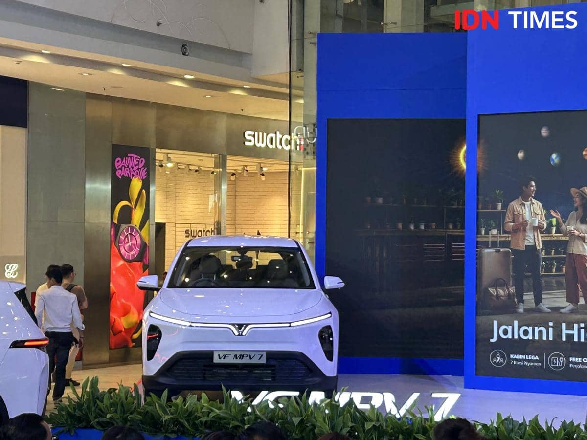 Mobil VinFast MPV 7 berwarna putih dipamerkan di sebuah pusat perbelanjaan dengan latar belakang papan promosi berwarna biru.