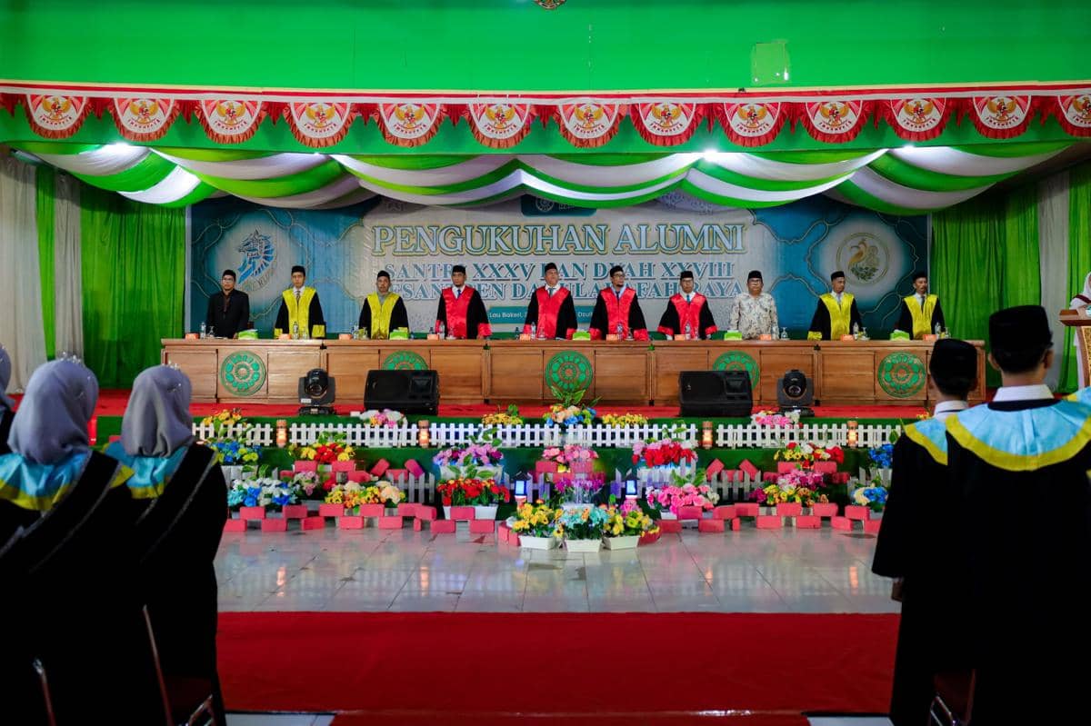 Upacara pengukuhan alumni Pesantren Darularafah Raya dengan para pengurus dan santri mengenakan toga di aula yang dihiasi warna hijau dan merah.