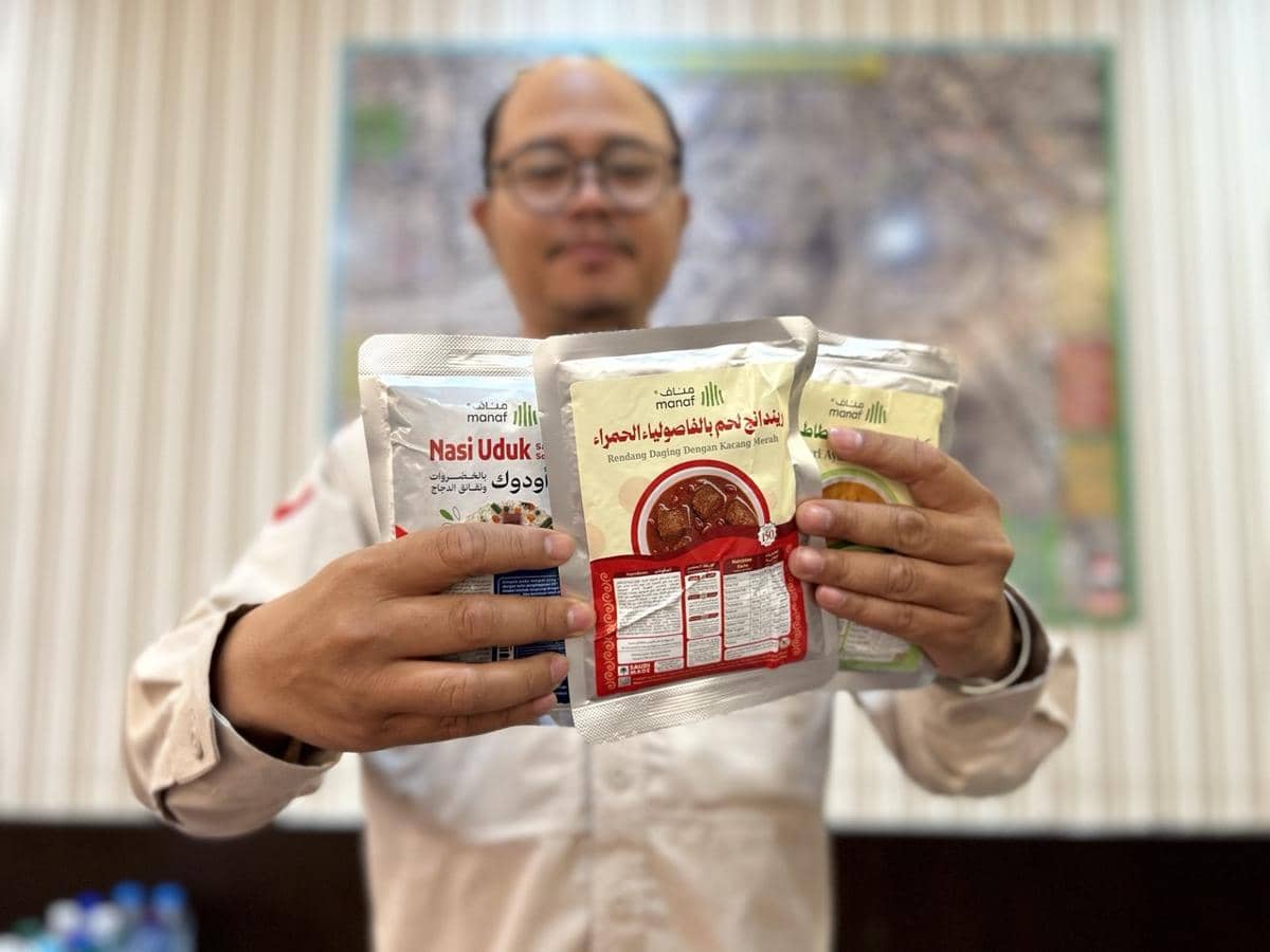 Seorang pria memegang tiga kemasan makanan siap santap merek Manuf, termasuk varian nasi uduk dan rendang daging dengan kacang merah.