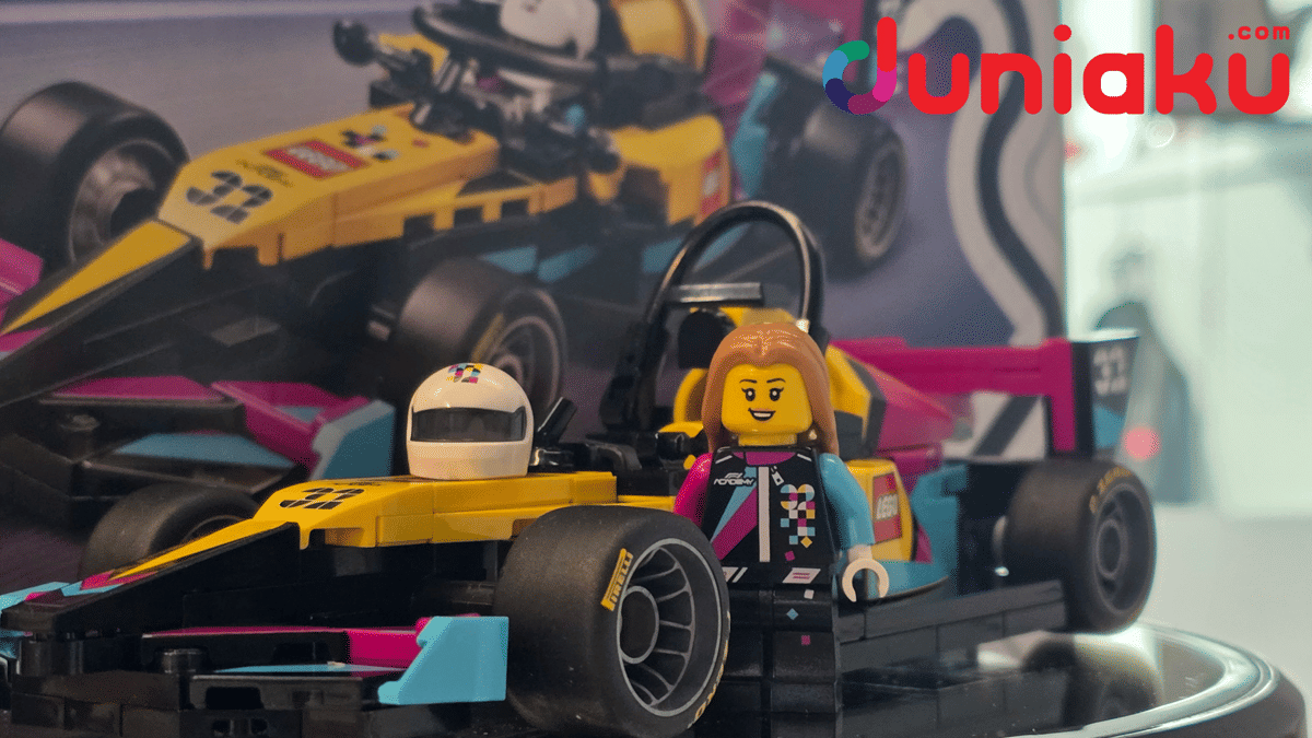 Mobil balap LEGO Speed Champions F1 Academy dengan minifigur pembalap perempuan berdiri di sampingnya di atas meja pajangan.
