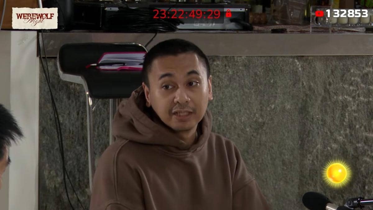 Seorang pria mengenakan hoodie cokelat sedang berbicara di depan mikrofon dalam acara Marapthon Season 3 di YouTube.