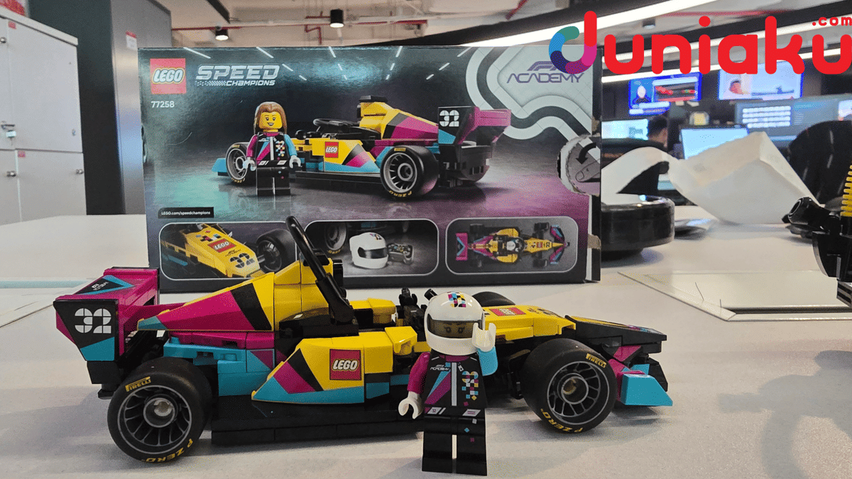 Mobil balap LEGO Speed Champions F1 Academy dengan warna kuning, merah muda, dan biru, disertai minifigure pembalap di atas meja kantor.