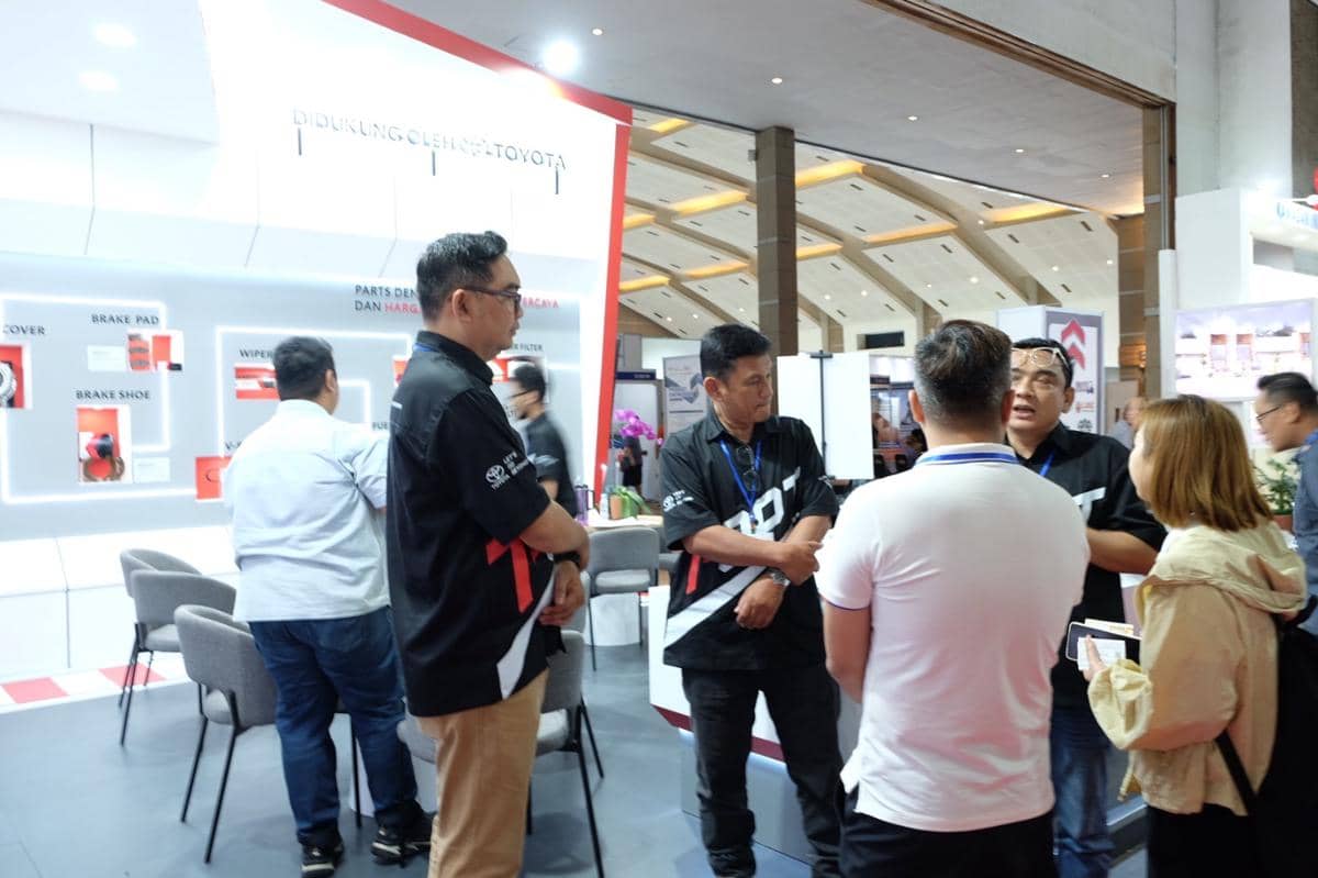 Beberapa orang berdiskusi di stan pameran Toyota dengan latar belakang display suku cadang kendaraan dan logo Toyota.