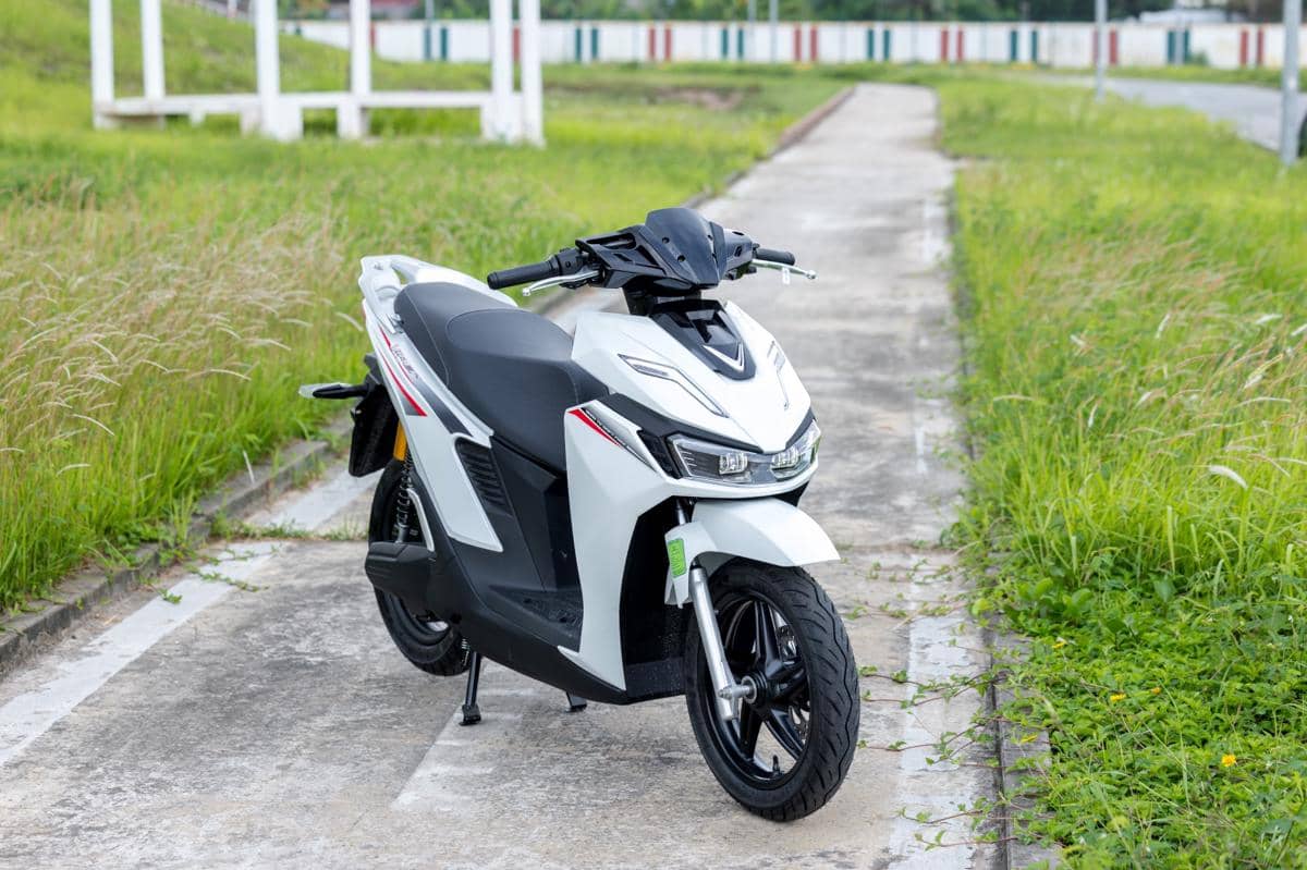 Motor listrik VinFast berwarna putih dengan desain modern diparkir di jalan beton di tengah area berumput hijau.